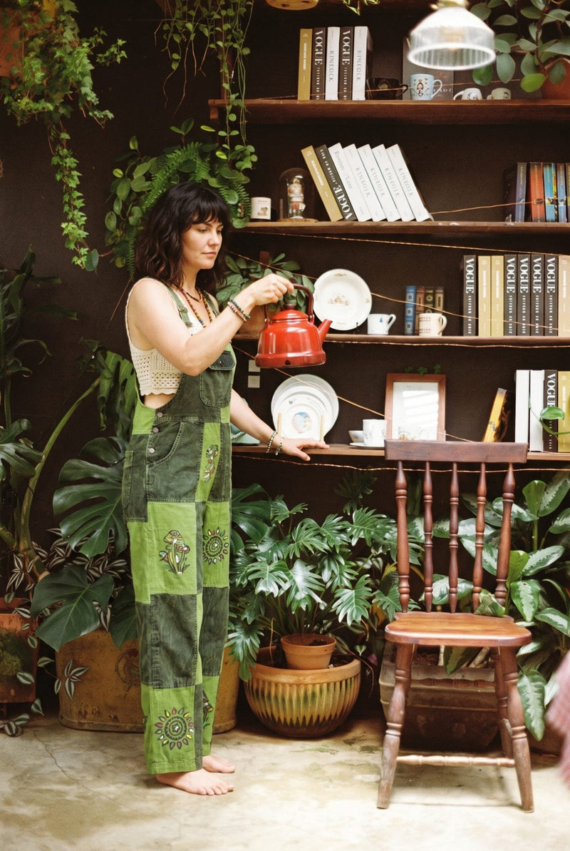Sungrove Overalls in side profile while pouring a kettle, mushroom and sunburst prints down the leg.