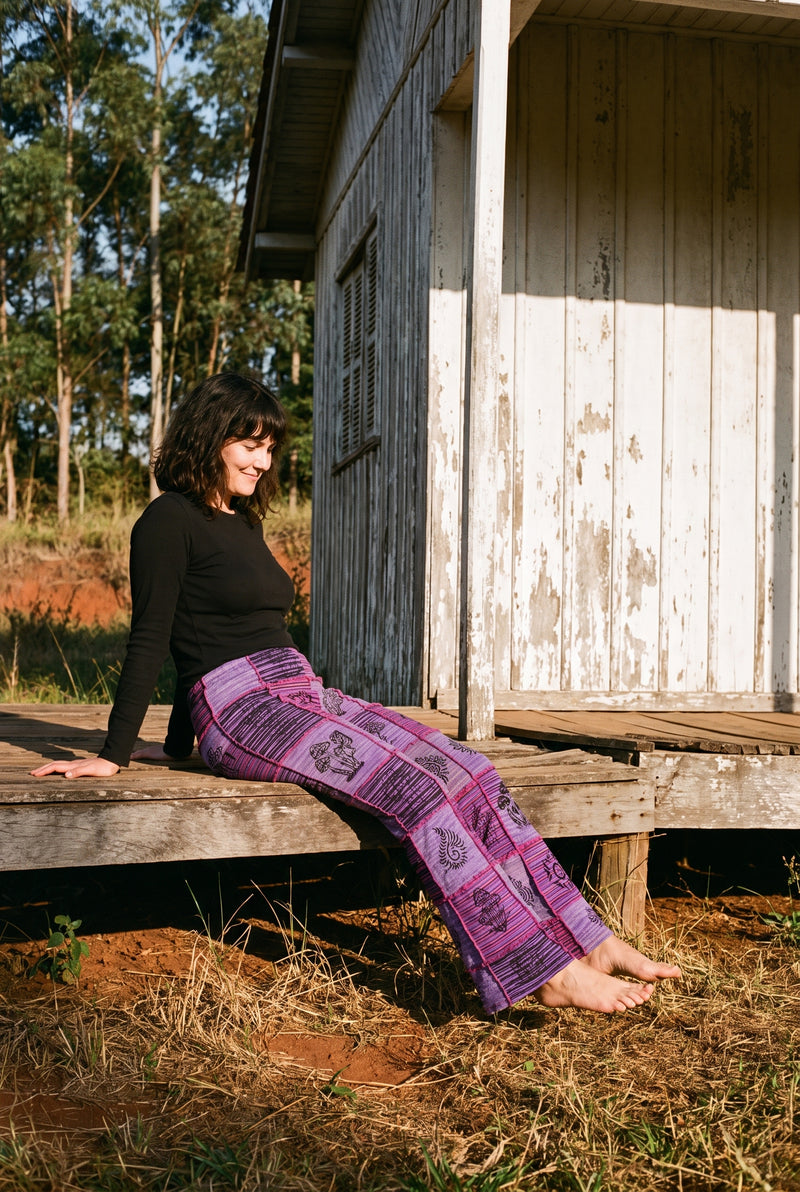 Mossgrove Patch Flares — Purple colourway, violet-lilac patchwork with magenta seams, seated at the farm cottage.