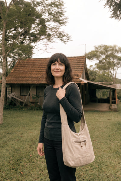 The Nomad Hemp Sling Bag in Natural worn over the shoulder: herringbone weave, front zip pocket and timber bead pulls.