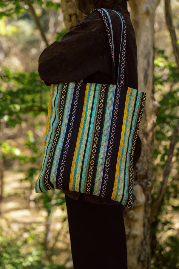 Black suede flap with woven body in turquoise, gold, white and black geometric striped pattern.