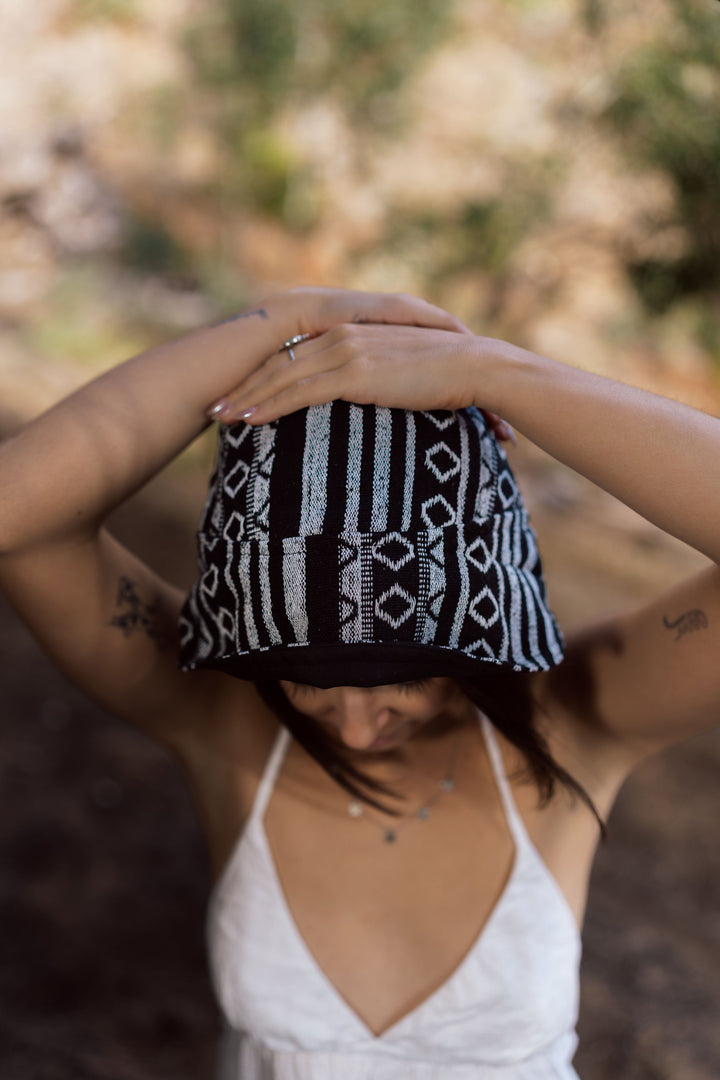 Black and grey knitted Nepali Nights Bucket Hat with vertical stripes and geometric diamond pattern, held by wearer's hands.