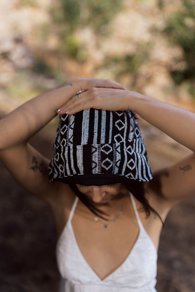 Black and grey knitted Nepali Nights Bucket Hat with vertical stripes and geometric diamond pattern, held by wearer's hands.