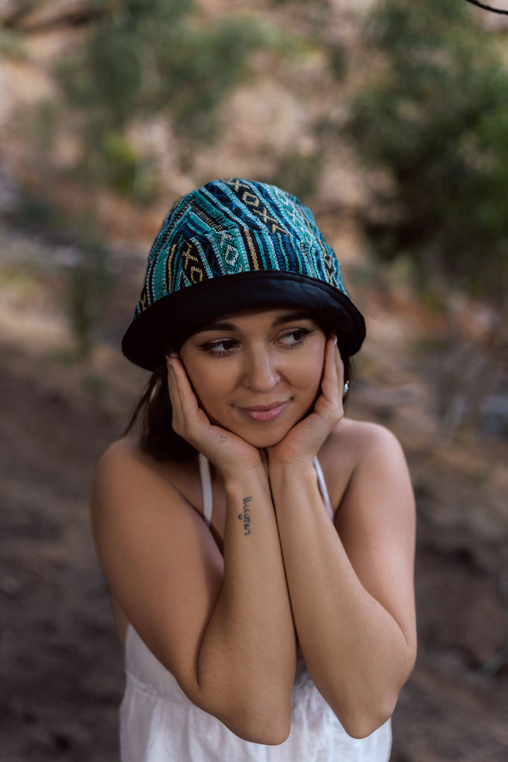 Turquoise knit bucket hat with black and gold geometric patterned crown and black brim.