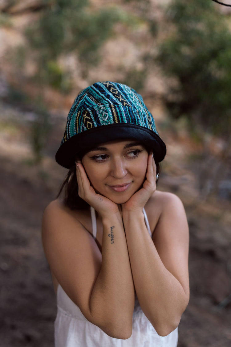 Turquoise knit bucket hat with black and gold geometric patterned crown and black brim.