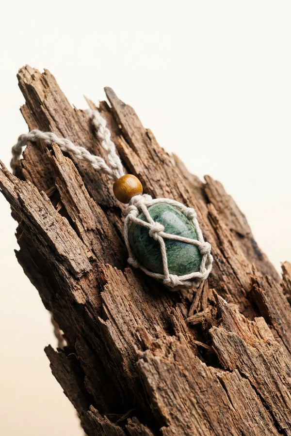 White Stonekeeper Necklace with green stone in cream rope net and golden bead on driftwood.
