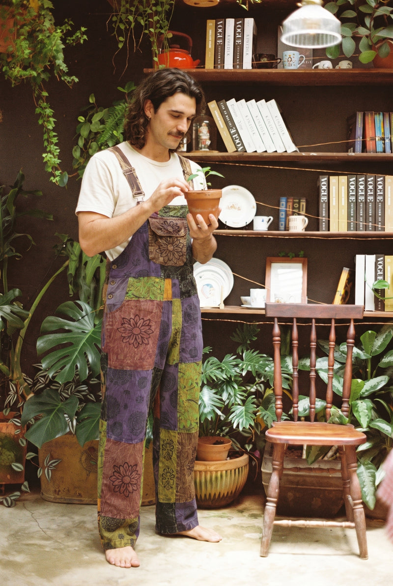 Close view of the Duskwood Overalls bib pocket and adjustable straps as a man tends a terracotta pot of seedlings