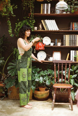Sungrove Overalls in side profile while pouring a kettle, mushroom and sunburst prints down the leg.