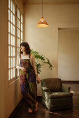 Duskwood Overalls in a wider room shot, purple, olive and rust patchwork with a floral-stamped chest pocket.