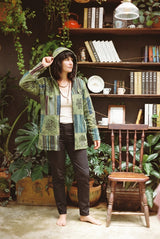 Green Horizon Patchwork Jacket worn open with the hood up, arm raised, green patchwork panels in view.