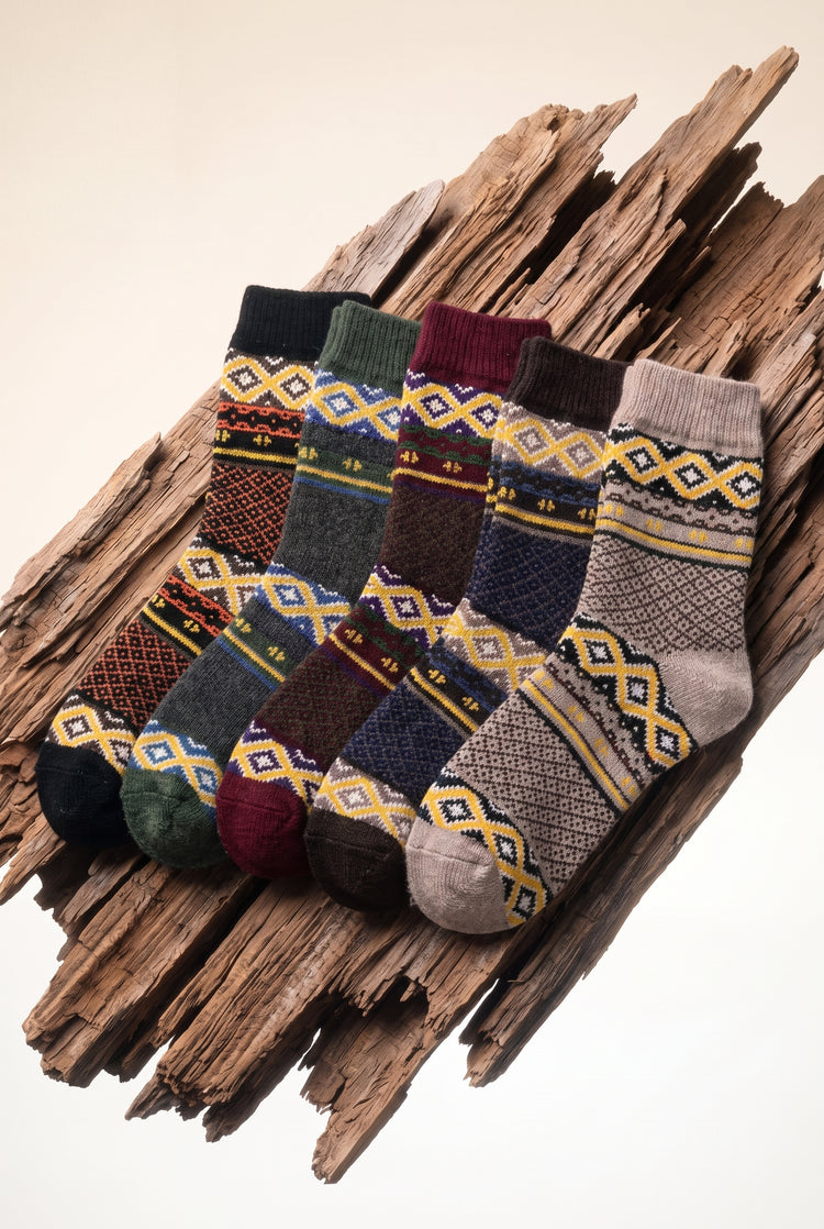 Highland Weave Socks 5 Pack, five Fair Isle wool blend crew socks in black, charcoal, burgundy, chocolate and oatmeal with mustard diamond bands, laid on a driftwood plank.