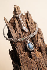Labradorite Moon Choker with flashing labradorite stone in pale grey macramé cord, silver beads and pearl closure, hanging on weathered driftwood.