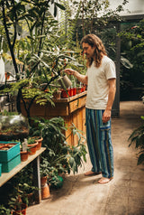 Side view of the Riverstone Gheri Cargo Pants showing the leg drape and buttoned side pocket, in a sunlit greenhouse