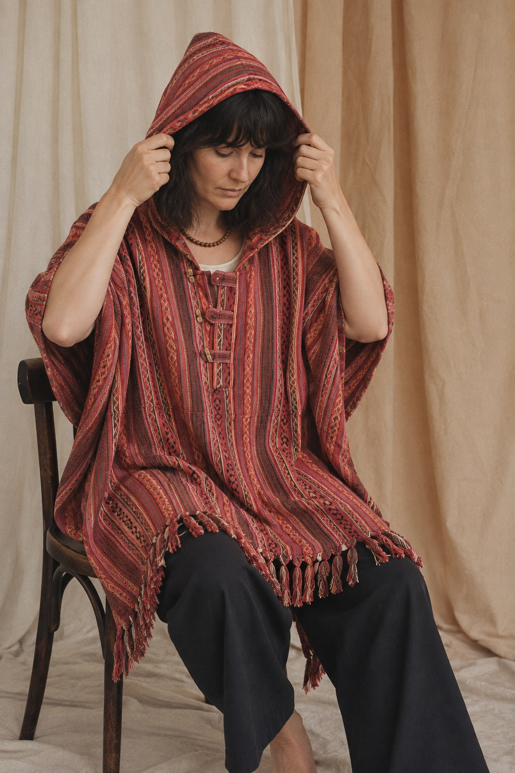 Rosewood Gheri Poncho, red, pink and rust stripe, worn with the hood up by a model in the calico studio