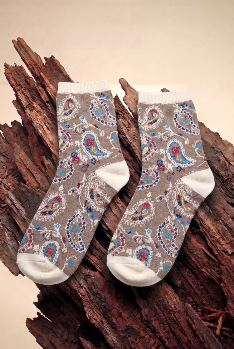 Sandstone Hippie Socks - taupe paisley crew socks with cream cuff, heel and toe, laid on driftwood