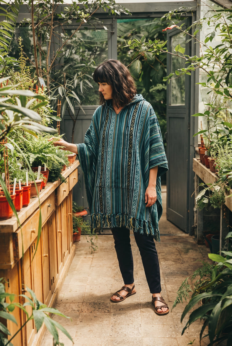 Woman reaching for ferns along a greenhouse bench, showing the drape and length of the fringed Tidewater Gheri Poncho