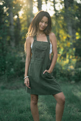 Olive green sleeveless Rainforest Dress with embossed geometric front pocket and shoulder straps, layered over white lace.