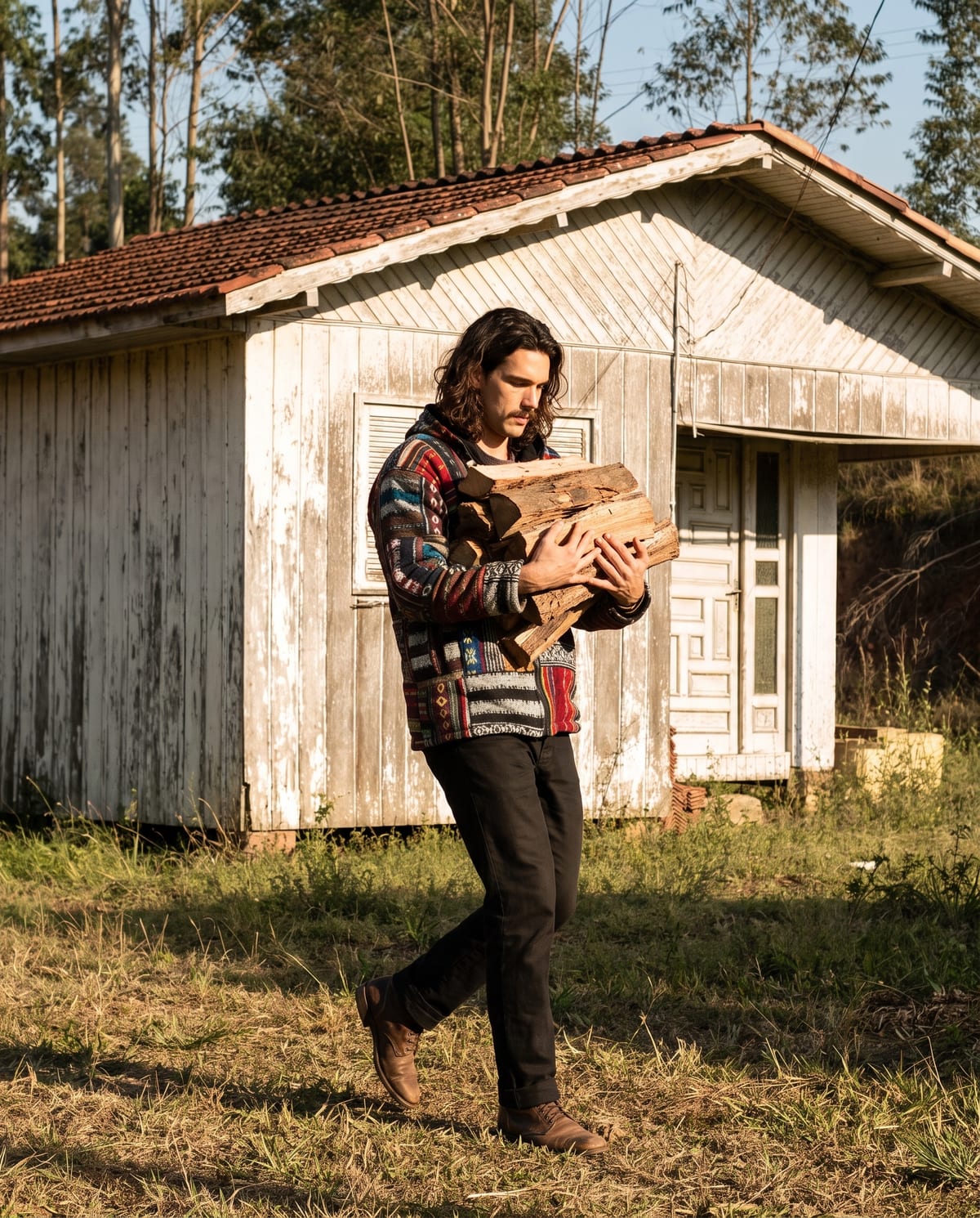 Model in a patchwork jacket carrying firewood past the weatherboard farmhouse