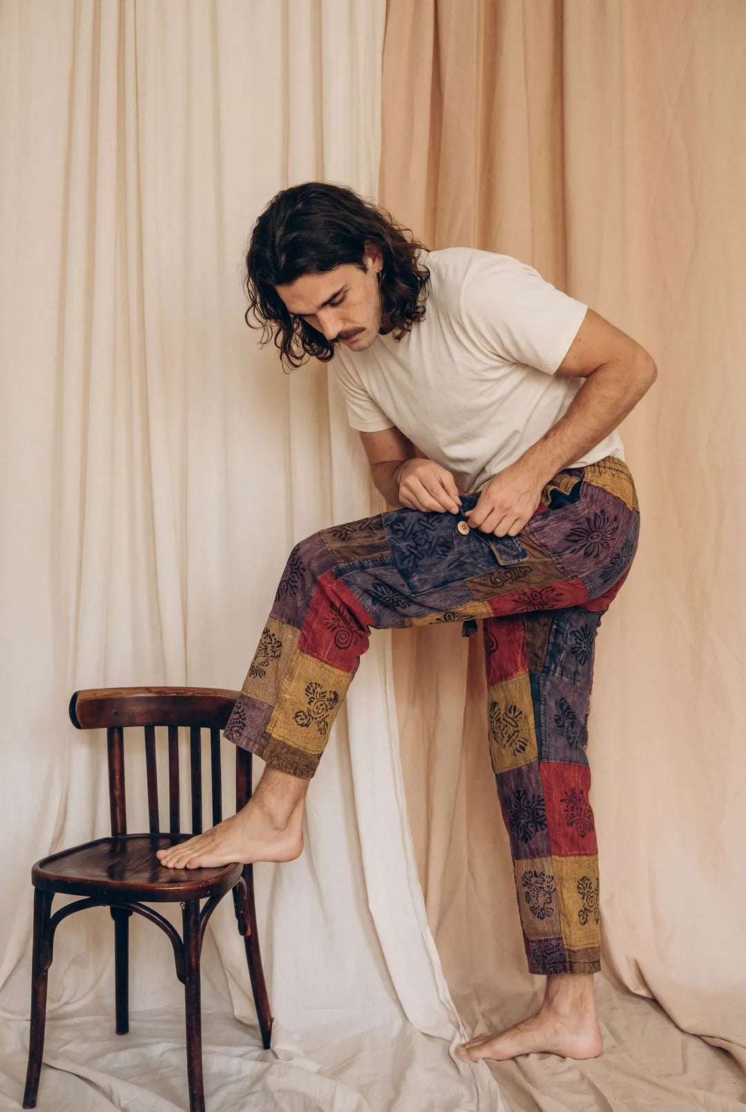 Emberglow Patchwork Pants, rust, mustard, plum and indigo, worn by a model with one foot on a chair in the calico studio