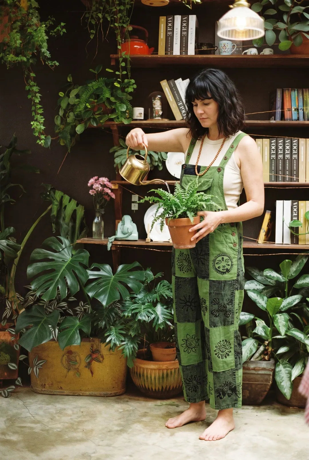 A model in Fernbrook Overalls holding a potted fern in front of a bookshelf