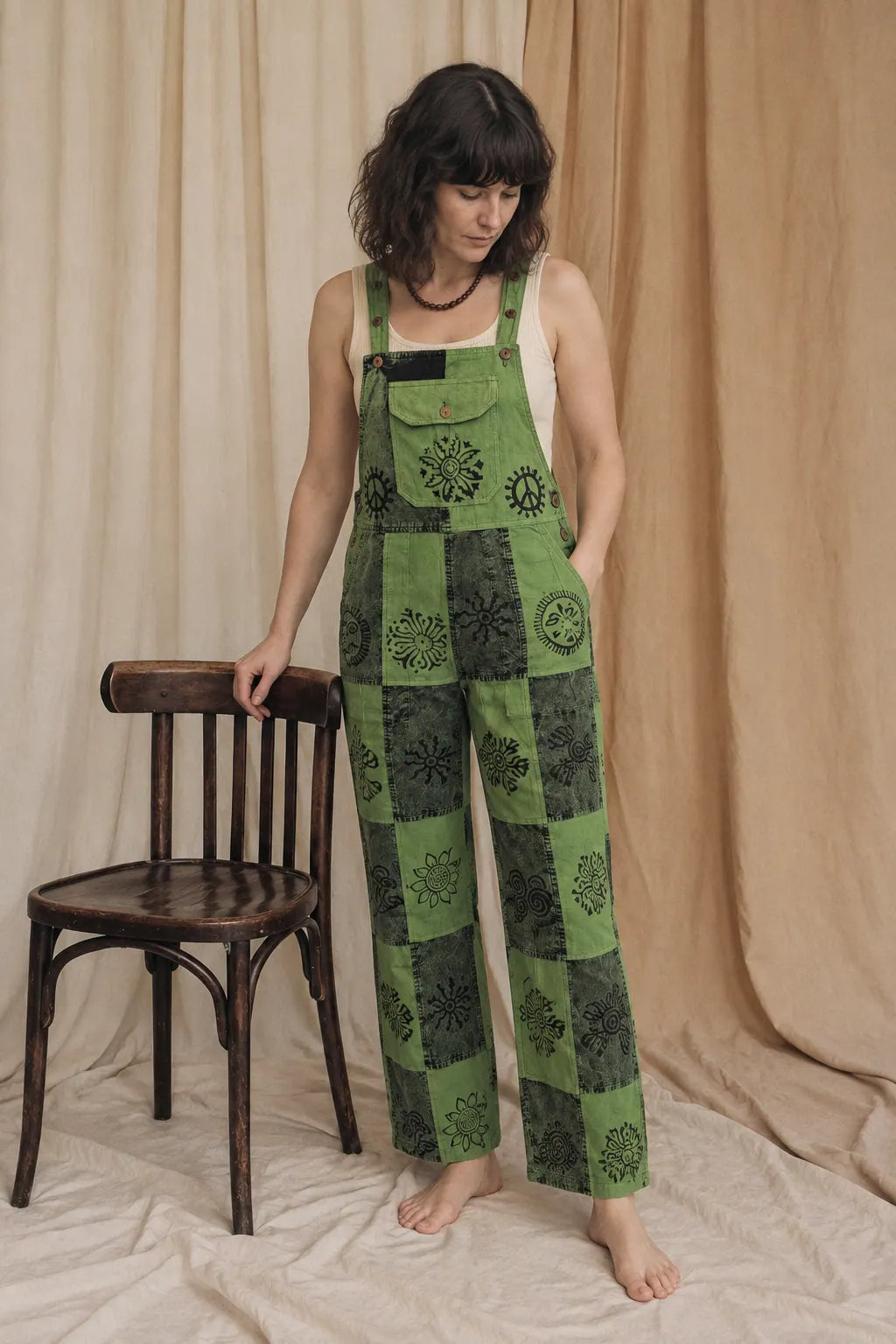Fernbrook Overalls, leaf and forest green, worn by a model standing beside a bentwood chair in the calico studio