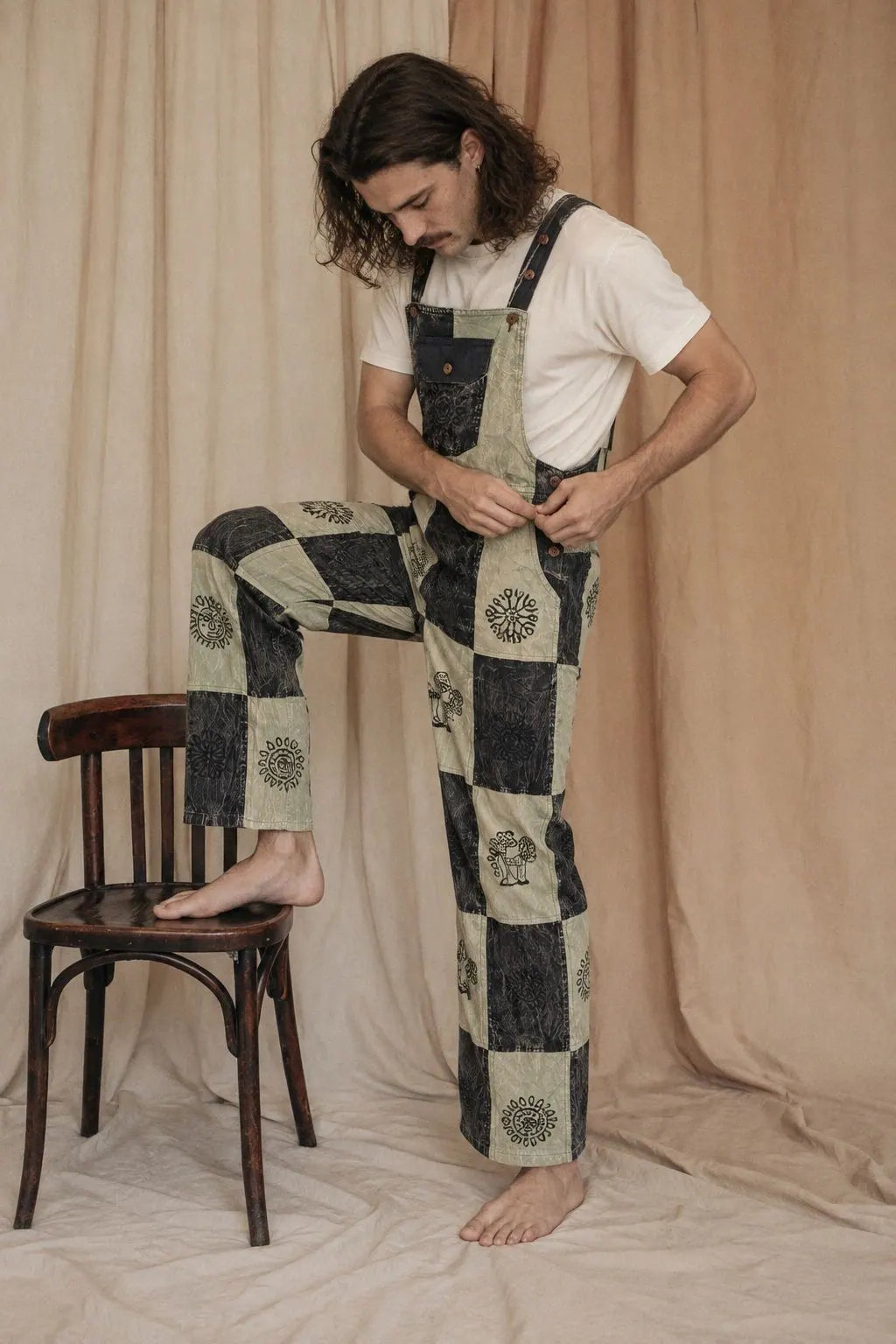 Mosslight Overalls, pale sage and black, worn by a model with one foot on a chair in the calico studio
