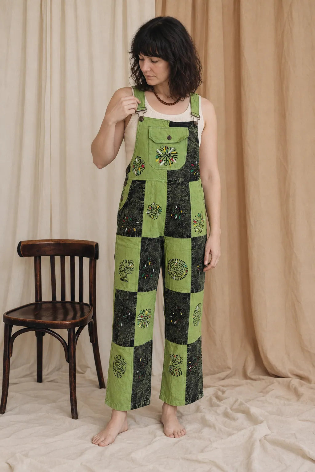 Sungrove Overalls, lime and dark forest green, worn by a model standing beside a bentwood chair in the calico studio
